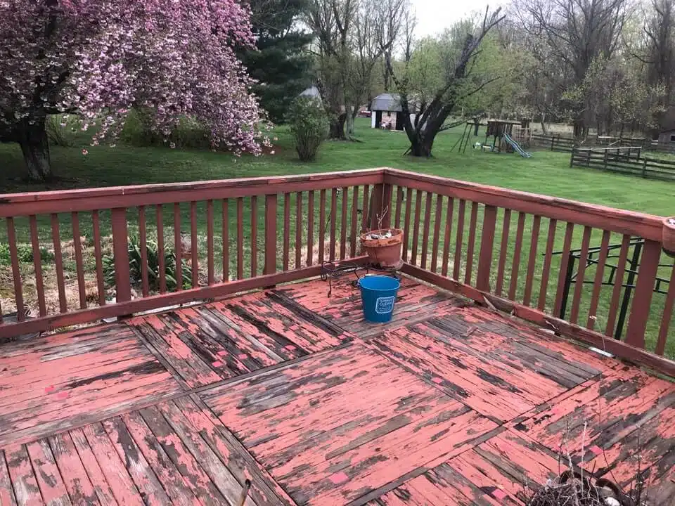Deck in need of restoration with peeling paint, surrounded by greenery and a flowering tree, illustrating the importance of professional deck services by Valentine Property Services.